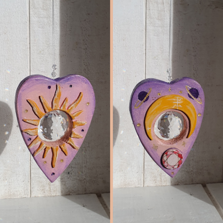 Attrape soleil Suspension décorative avec une goutte ouija taillée dans du bois et motifs soleil et lune pyrogravés. Un cristal suspendu au centre projette des arc-en-ciel sur un mur.