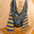 Photo de prêt montrant l'illustration d'Anubis avec de la pyrogravure et de la peinture sur une tranche de bois de bouleau. Les couelurs utilisées sont dans les bleus foncé et indigo, ainsi que du doré.